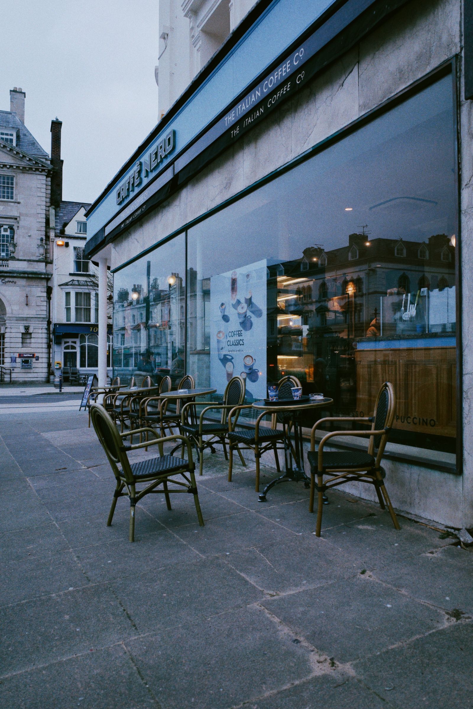 La terrasse du café, ses chaises en rotin tournées vers la place