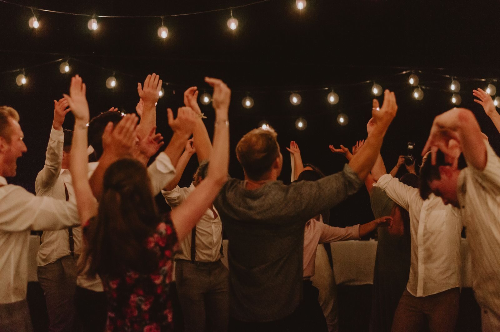 Les danseurs du bal, bras levés sous les guirlandes d'ampoules, un soir de fête